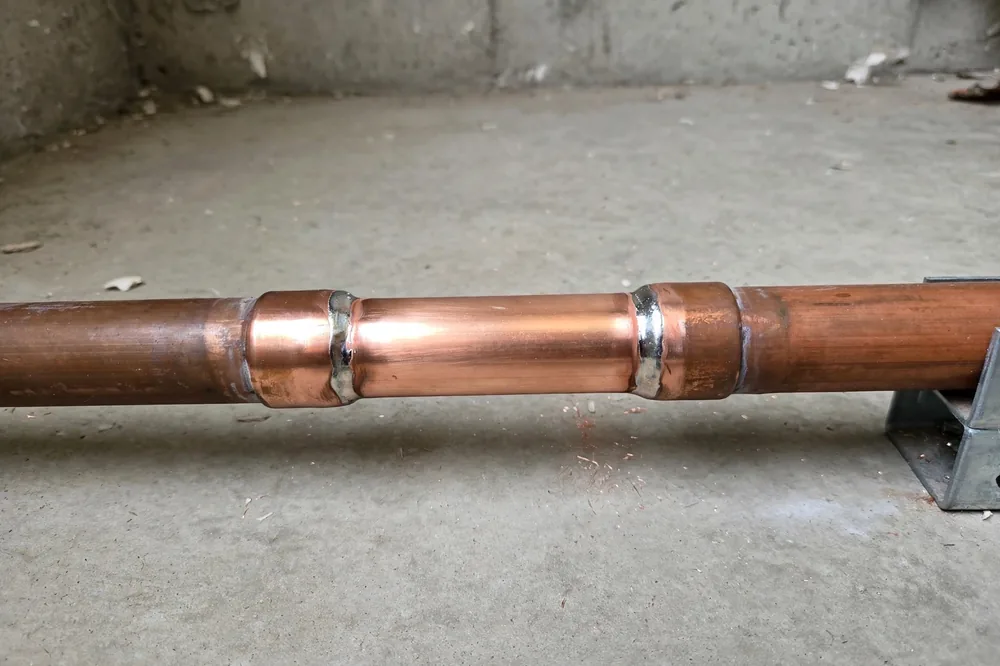 Clean new copper pipe section with neat soldered joints and a dry floor