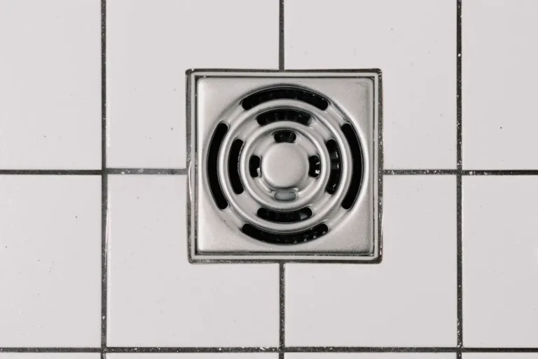 Free Top view of white ceramic tile floor with stainless steel square shaped cover of drain in contemporary shower Stock Photo