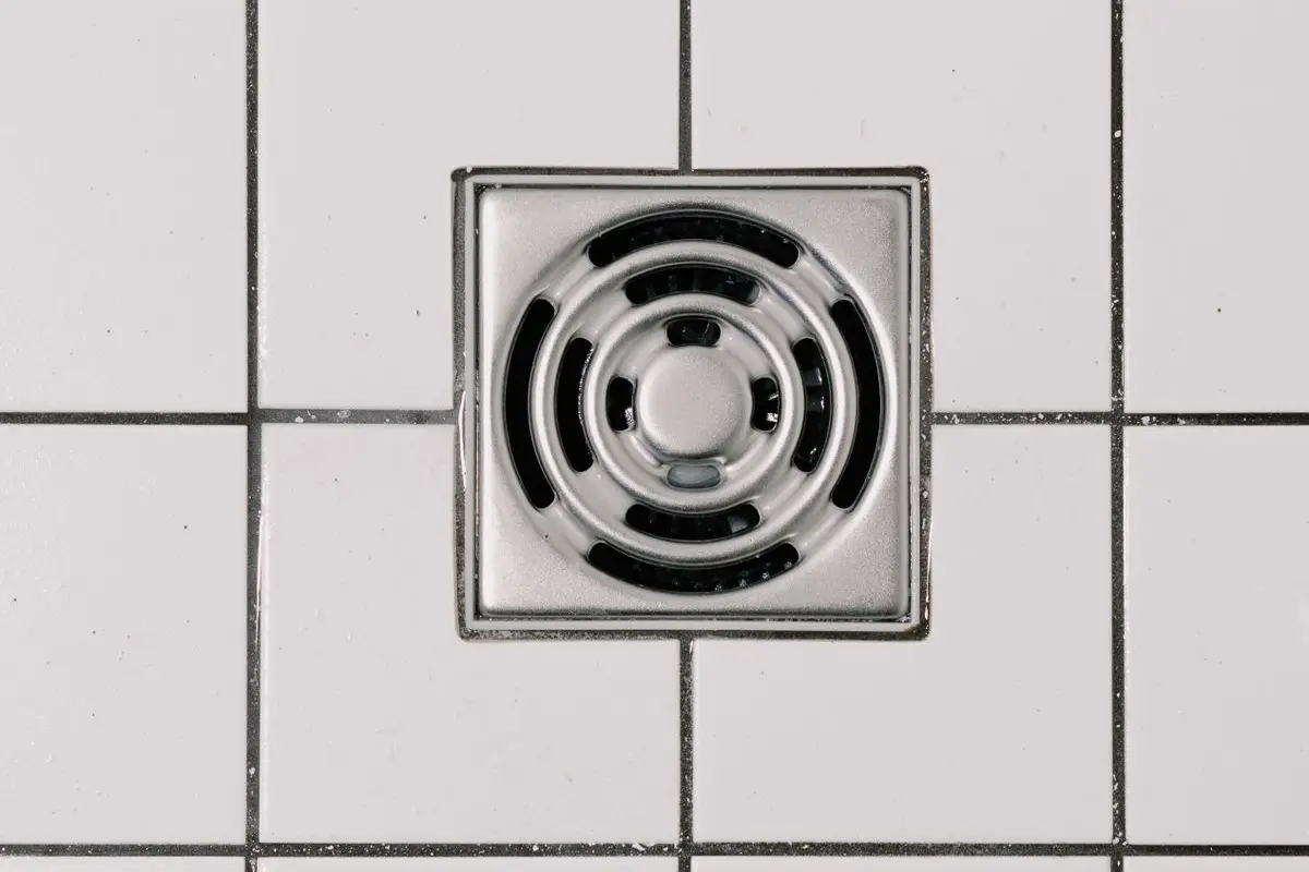 Free Top view of white ceramic tile floor with stainless steel square shaped cover of drain in contemporary shower Stock Photo