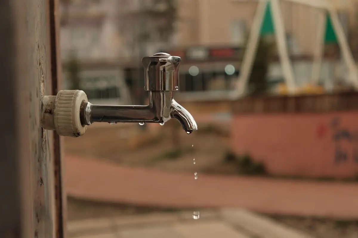 Free Close-up of a dripping outdoor water faucet with blurred urban background, creating a moody urban scene. Stock Photo