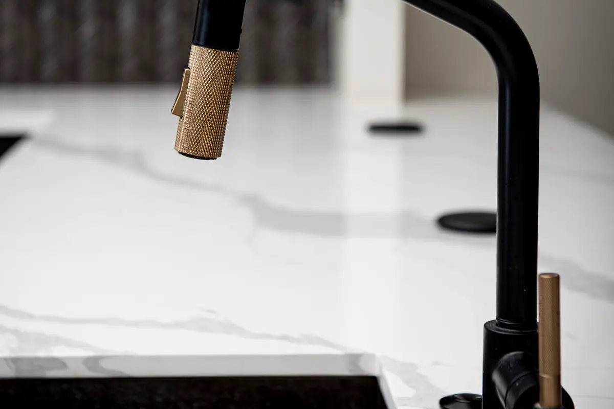 Modern black and brass pull-down kitchen sink faucet over a marble counter