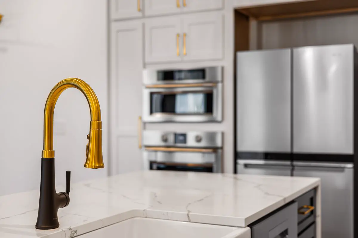 Gold gooseneck kitchen faucet on a white marble island in a modern kitchen