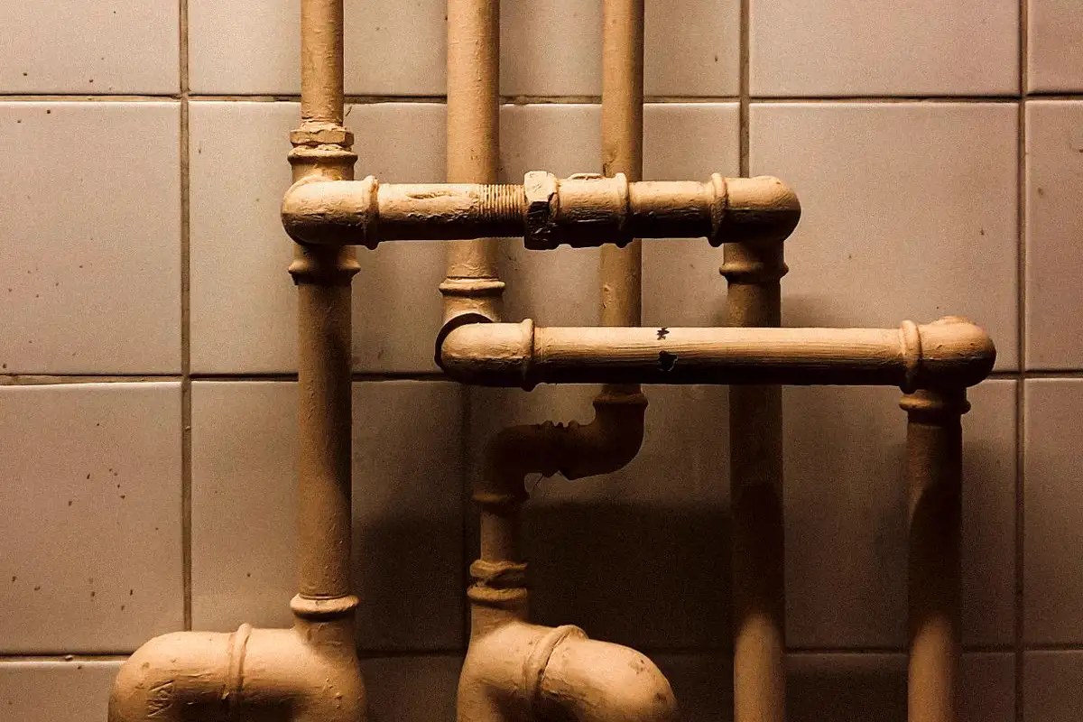 Free An artistic capture of vertical industrial pipes against a tiled wall, showcasing geometry. Stock Photo