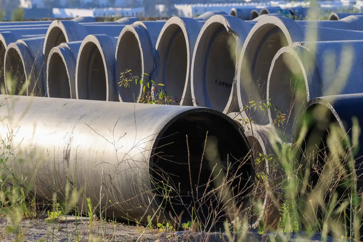 Free Stacked concrete pipes in an outdoor storage area surrounded by grass. Stock Photo