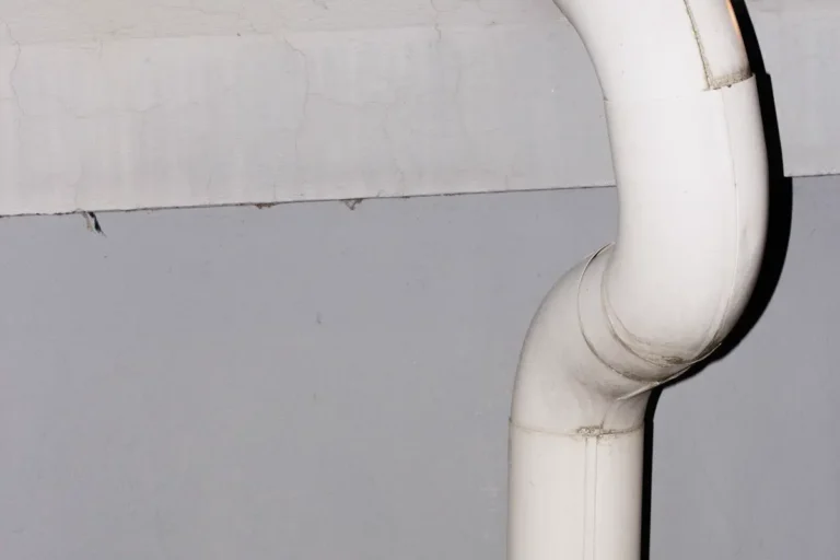 Free Vertical shot of a curved white drainage pipe against a concrete wall. Stock Photo